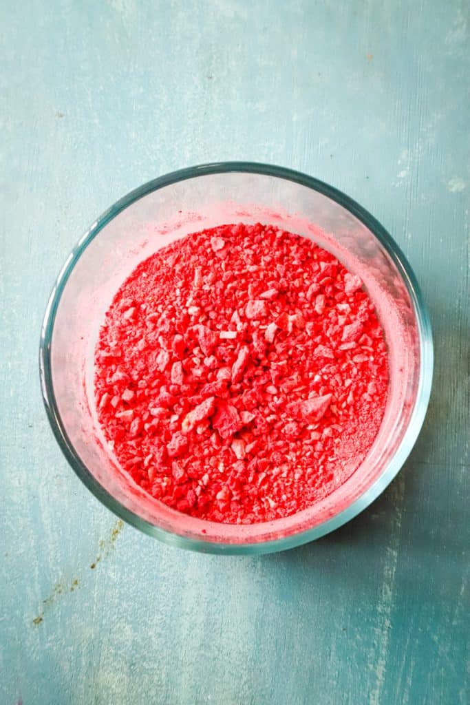 The crushed freeze dried strawberries in a small glass bowl on blue background.